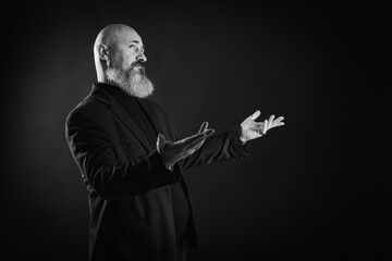 Smiling business man with beard showing man, gesturing with hands, showing something, isolated on dark background. Low key. The portrait is emotional