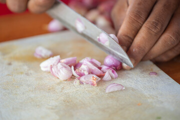 close up of a hand cutting white onions and chilli pepper on a kitchen board with a knife