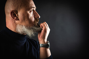 Frightened shocked worried bearded man, opened his mouth, holding his hands to his face, fingers in his beard, looking frightened in a panic, isolated on a dark background. Portrait, low key