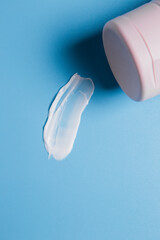 drop of white body cream smeared on a blue background next to a pink closed tube