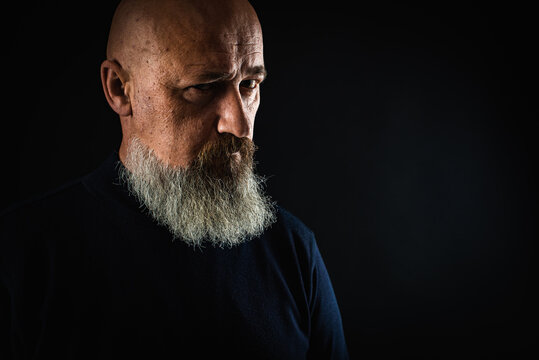 close up photo, portrait of a serious, thoughtful, bearded man on a dark background confident and dramatic looking straight. Concept of male portrait.  Low key 