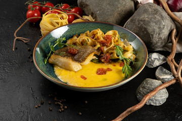 Fried halibut with tagliatelle and hollandaise sauce. Hot main course of fish fillet, boiled pasta and sauce with red caviar and microgreens.