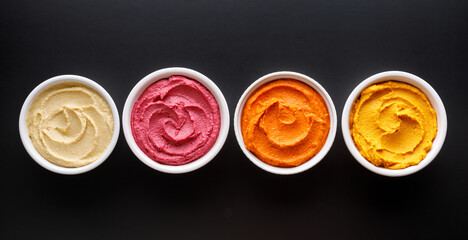 Set of different colorful hummus: classic, beetroot, pepper and pumpkin  on a black background top view