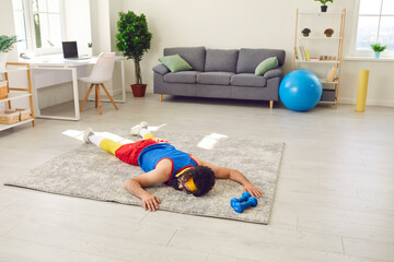 Tired exhausted young sportsman decided to take a break after failing to do push-ups during sports workout at home. Funny male athlete is lying on floor after giving up fitness training with dumbbells