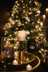 shiny christmas candles and glass champagne glasses on a gold tray against a sparkling christmas tree background, new year 2023, 2024