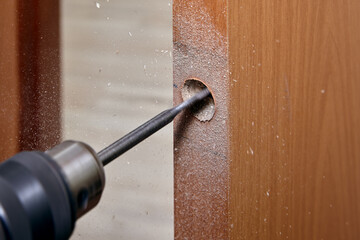 Carpenter drills hole for latch in new door.