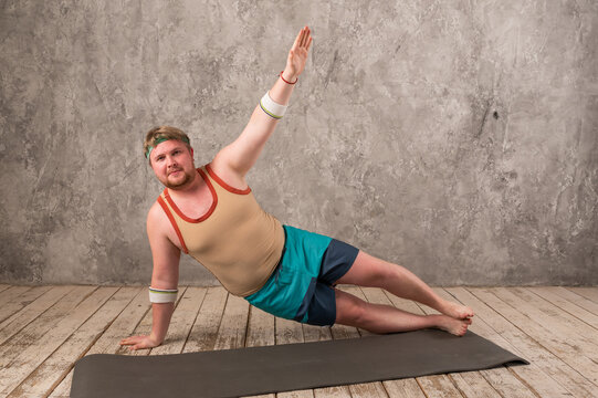  overweight man exercising, doing stretching exercises on yoga mat, watching fitness videos online on laptop at home. yoga exercises online with laptop