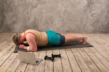  overweight man exercising, doing stretching exercises on yoga mat, watching fitness videos online on laptop at home. yoga exercises online with laptop