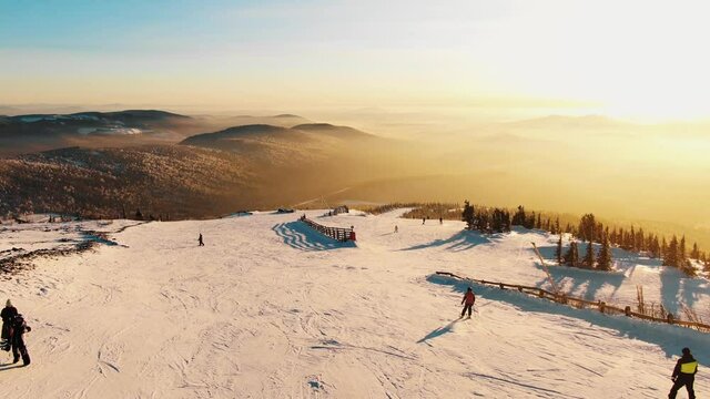 Amazing view from the air at sunset on the ski slope and mountain slopes bathed in magical light and rays of the sun. Vacationing hipsters on skis and snowboards in protective gear drive downhill