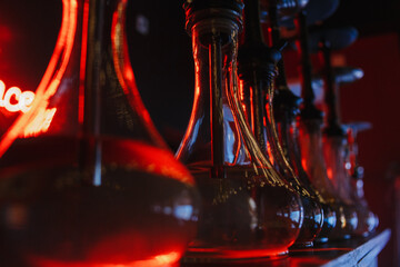transparent glass hookah flasks stand in a row against the background of a red neon inscription hookah place