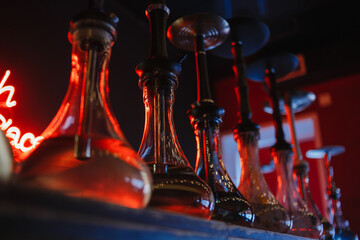 transparent glass hookah flasks stand in a row against the background of a red neon inscription hookah place