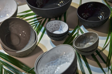 Different sizes and colours clay bowls in a set on the background of palm leaves. Selective focus.
