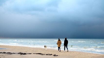 Walk in winter along the seashore. Young couple with a dog for a walk.