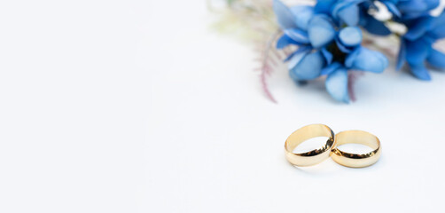 Blue flowers and two golden wedding rings on white background.	