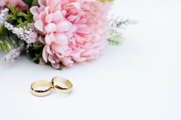 Pink flowers and two golden wedding rings on white background.	