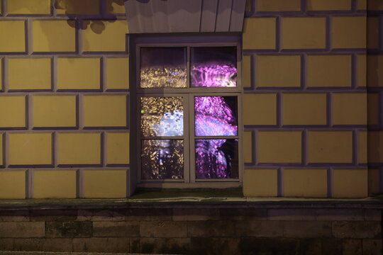 One window on the facade of the building glows with a festive light in the dark.The glass reflects the fireworks in gold and purple colors