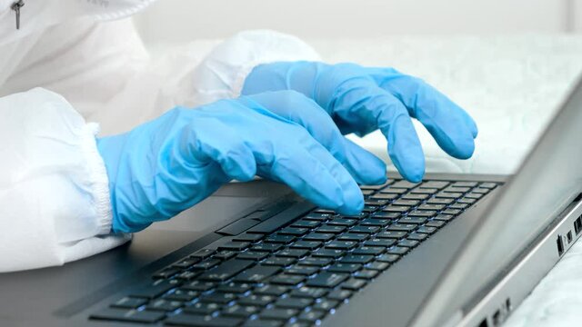 Closeup of doctor in medical protective gloves typing on laptop keyboard. People protecting from covid-19 and coronavirus while working remotely