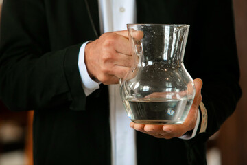 Man holding in his hands a transparent jar filled with water to be blessed during a baptism in the Christian religion