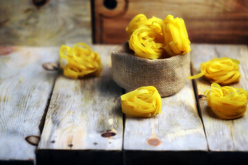 Fototapeta na wymiar Raw fetuccine pasta on a wooden surface. Nest paste. Italian Cuisine. Selective focus.