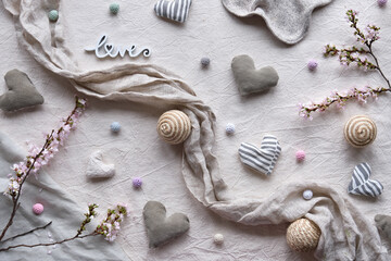 Fototapeta na wymiar Hand made linen hearts and balls on linen background. Textile handicraft in neutral colors. Springtime flower twigs. Hand hold soft heart. Monochromatic, desaturated colors. Rustic seasonal decor.