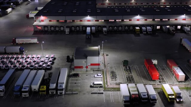 Logistics park with warehouses, loading hub and a lot of semi-trailer trucks waits for load and unload goods at ramps. Aerial view at night
