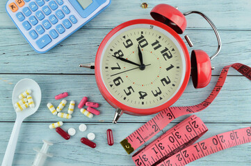 Capsules or pills on white spoon, syringe, alarm clock, calculator and measuring tape isolated on wooden background. Slim by pills, dangerous for health. Diet concept.
