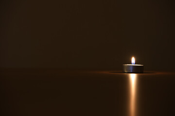 Closeup shot of a burning small candle with a light reflection on a table surface
