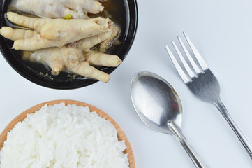 The crop image of white rice, chicken feet spicy soup, fork and spoon isolated on a white background. Famous Asian food.