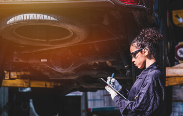 Engineer car mechanic under checking under the car by see detail in note book on hand for maintenance and fixed it.