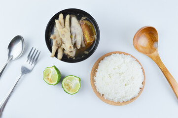 Flat lay view of chicken feet spicy soup with white rice, fork, spoons and Kaffir lime isolated on a white background. Famous Asian food.