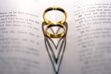 Closeup of wedding rings forming heart shapes on the bible - concept of love and marriage