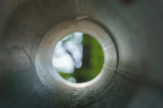 looking into a metal pipe with blur green tree at the end