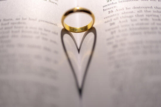 Closeup of a golden engagement ring forming a shadow of a heart on the open holy bible