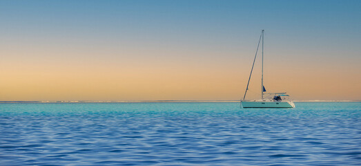 A sailboat on blue ocean water during a beautiful sunset