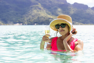 Happy woman in tropical island Bora Bora lagoon turquoise ocean water drinking champagne while on a sunshine filled vacation with Mt. Otemanu in the background