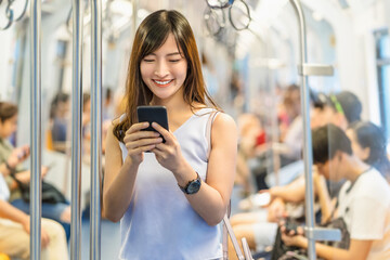Young Asian woman passenger using social network via smart mobile phone in subway train when...