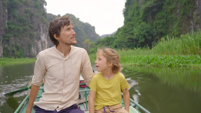 A young man and his son on a boat having a river trip among spectacular limestone rocks in Ninh Binh, a tourist destination in northern Vietnam. Travel to Vietnam concept