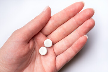 Female hand on white background holds two white pills. Dose of medicines.