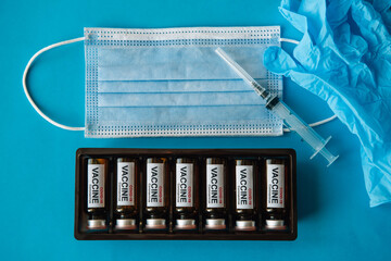 Naklejka premium Vials with vaccine, syringe, gloves and face mask on blue background, close up. Vaccination coronavirus covid-19 and immunity improvement.