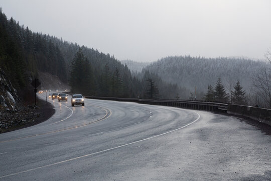 A picturesque daytime view of cars on a freeway flanked by snow dusted mountains and pine trees - Oregon