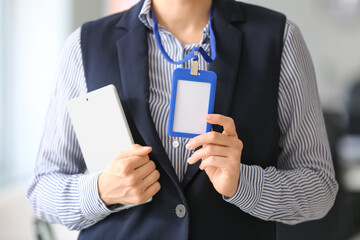 Young woman with blank badge and tablet computer in office, closeup