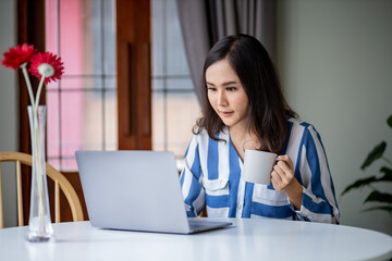 beutiful woman working on laptop in the room while hold a cup of  coffee.