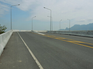 Fototapeta premium Open road on the bridge with mountain and blue sky in background, Southeast Asia, Thailand