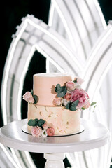 delicate beige wedding cake decorated with delicate pink yellow roses and eucalyptus on a black background