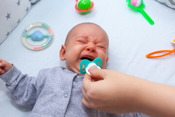 hand holds out a pacifier to a crying newborn. Selective focus