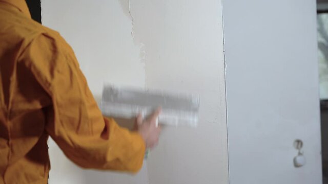 Plasterer man putty the wall with putty, leveling the wall, close-up hands.