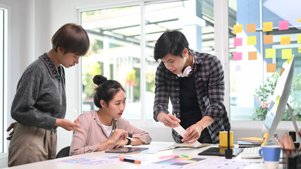 Group of designers in casual clothes working on project together and sharing ideas at creative office.