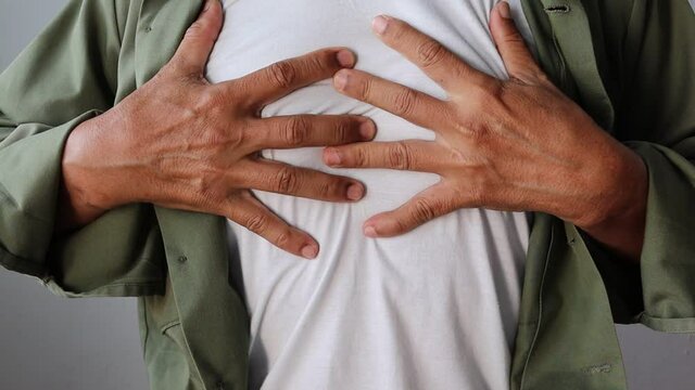 Man in shirt holding his chest with both hands, with severe pain isolated on white background closeup. 