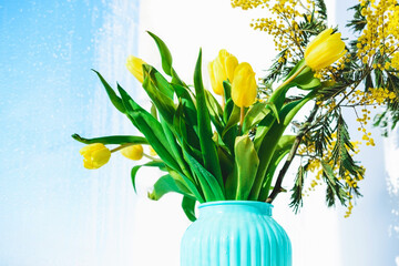 Bouquet of yellow tulips and mimosa in a vase.