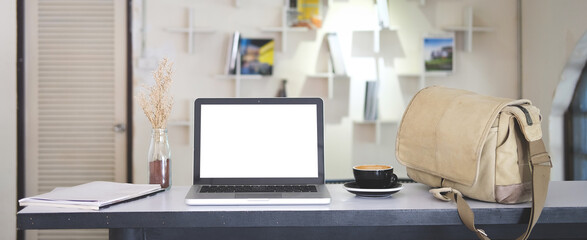 Mock up laptop computer with blank screen, coffee cup and notebook on modern workspace.